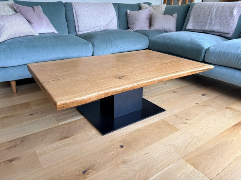A solid French oak coffee table with a live edge on a black Virelli plinth base, in a living room