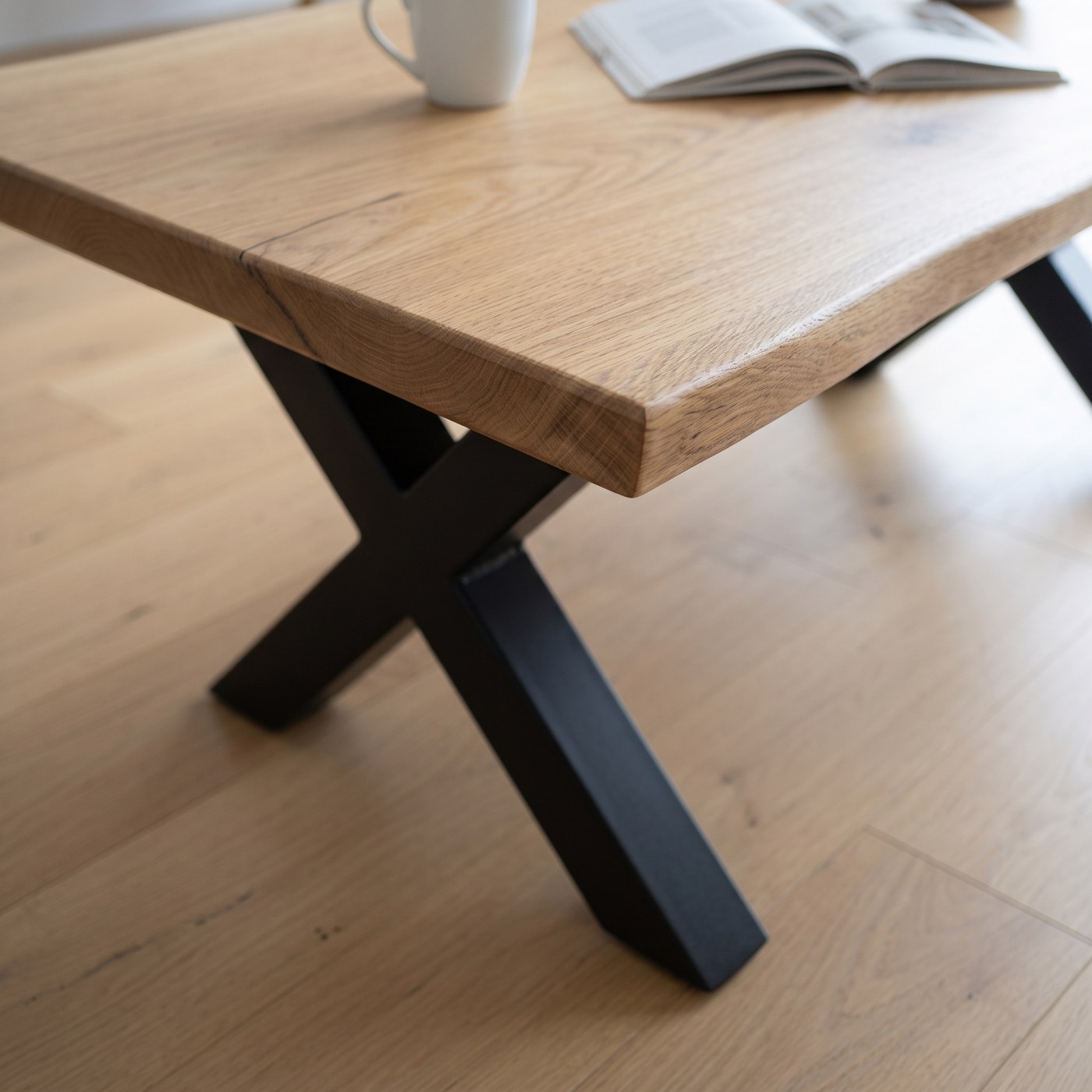 The live edge and corner of a solid French oak coffee table above its black steel X leg