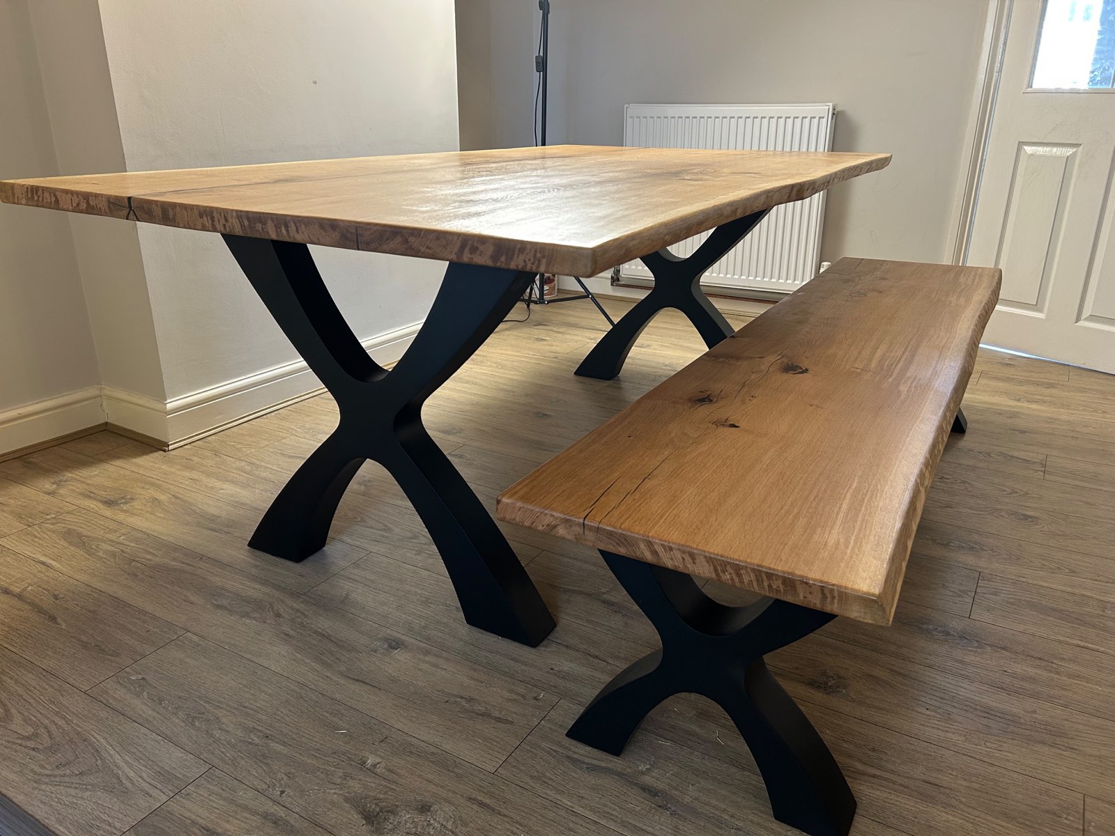 Solid French oak dining table and matching bench with black Designer X legs, seen from the kitchen doorway