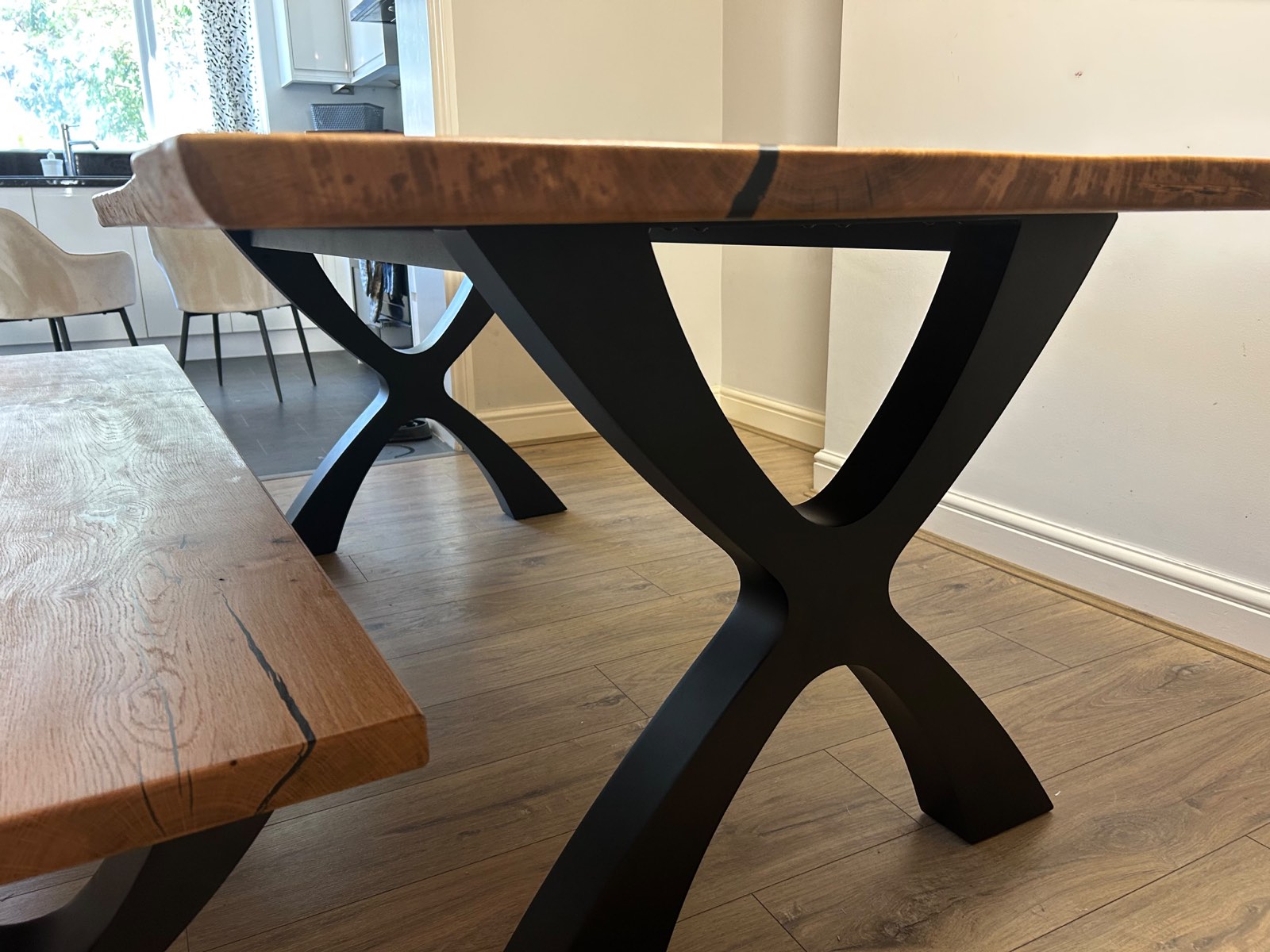 Close view of the sculpted black Designer X steel leg beneath the live edge of the oak top