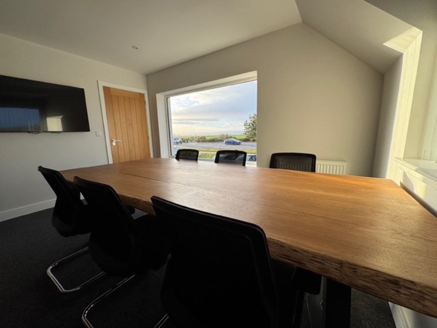 A bespoke live-edge oak meeting table in a private office overlooking a coastal view