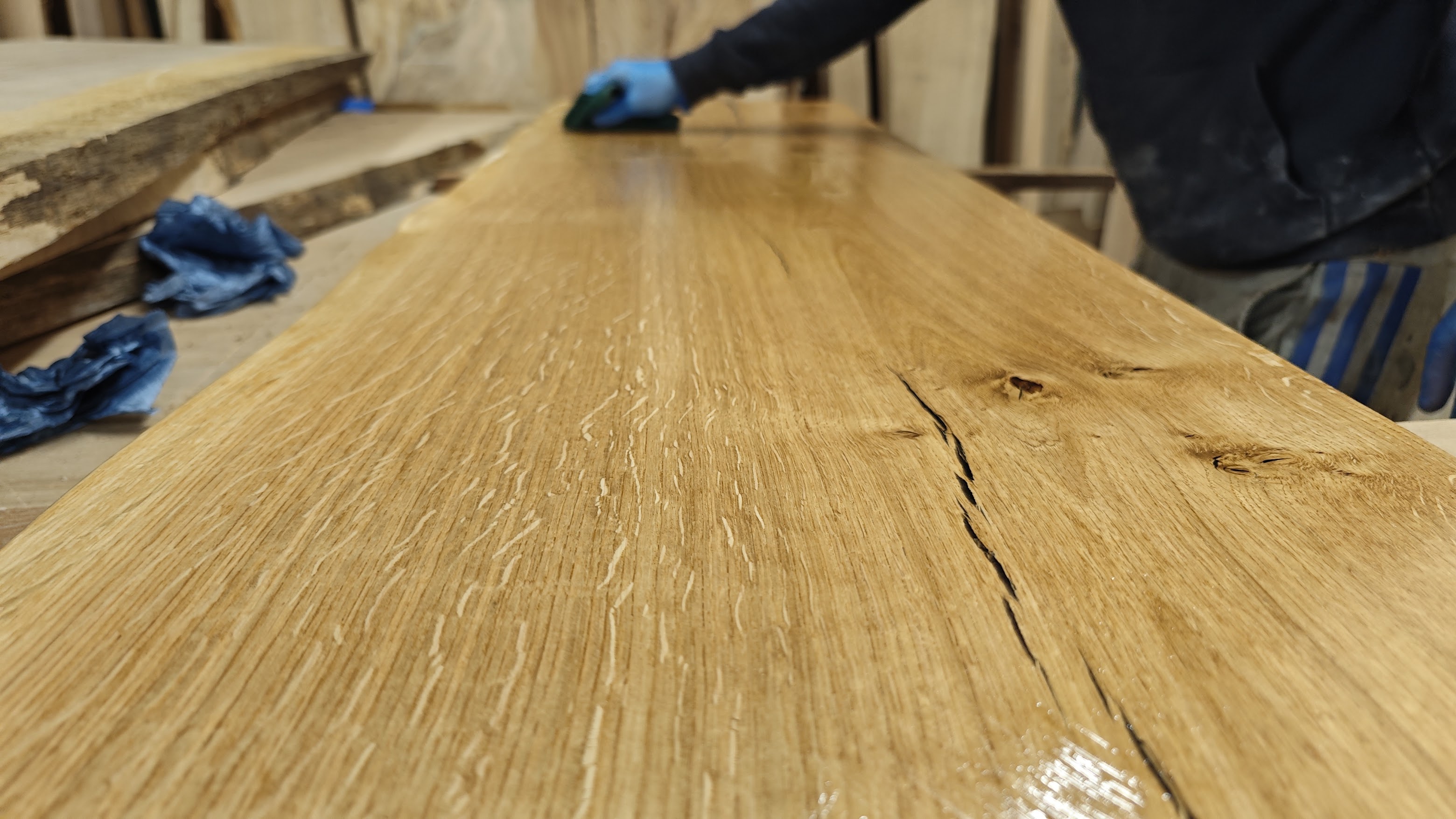 A maker meticulously finishing a French oak tabletop with food-safe hardwax oil in the Essex workshop, showing the deep grain pattern come alive