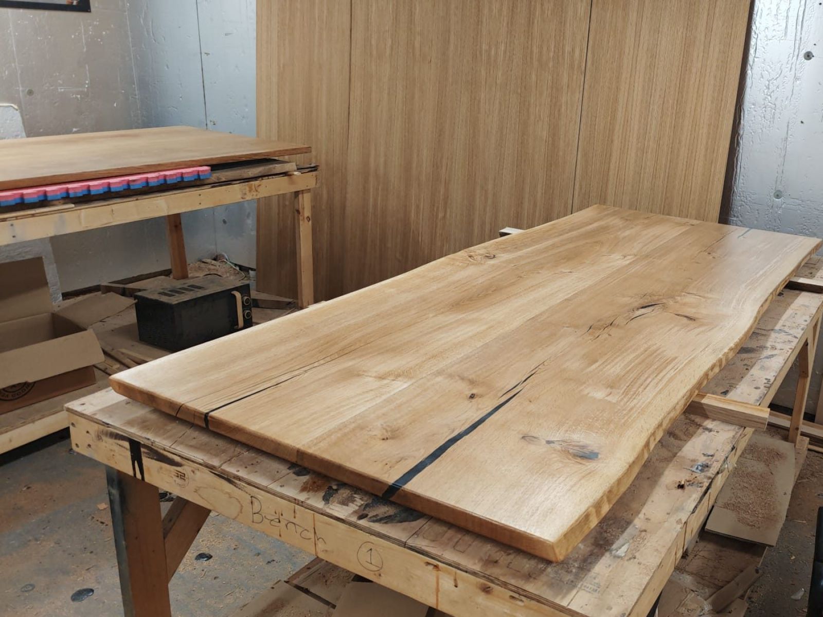 A finished live-edge French oak tabletop on the workshop bench, its natural split filled with black resin